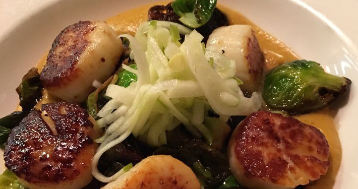 Seared sea scallops with shaved fennel and roasted brussels sprouts on a white plate.
